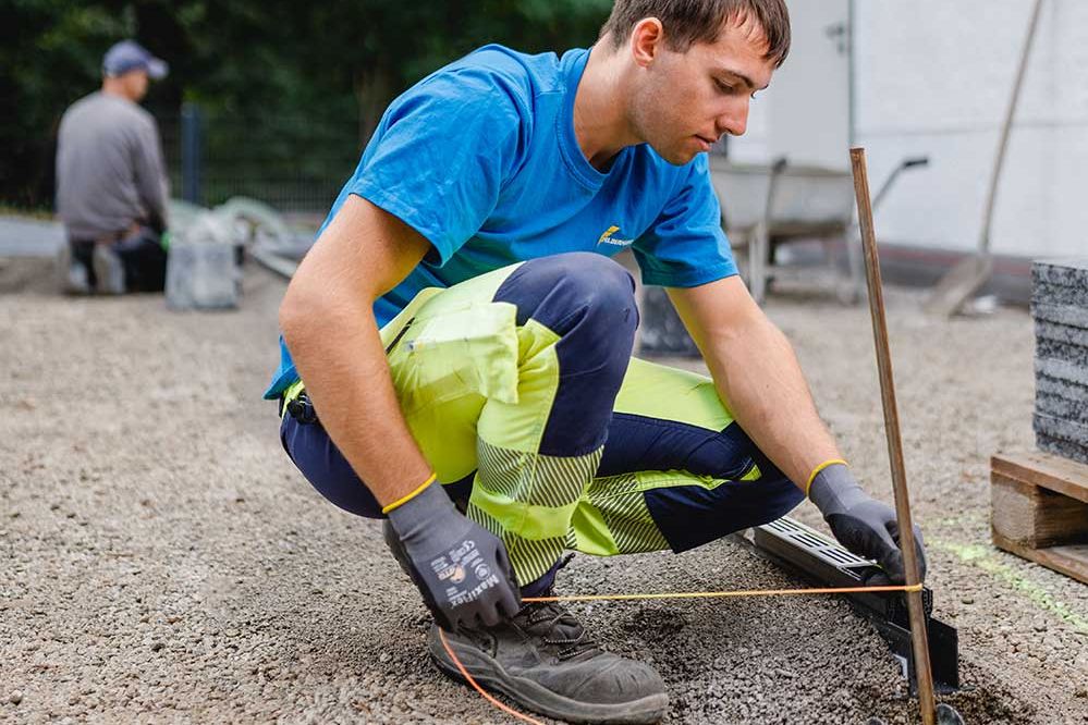 Lehre als Pflasterer: Ein Lehrling fixiert die Richtschnurr an einer Eisenstange auf der Baustelle