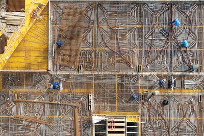 Luftaufnahme einer Baustelle mit dicht verlegten Rohrleitungen für eine Betondecke und mehreren Personen, die an der Konstruktion arbeiten.