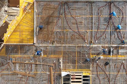 Luftaufnahme einer Baustelle mit dicht verlegten Rohrleitungen für eine Betondecke und mehreren Personen, die an der Konstruktion arbeiten.