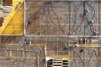 Luftaufnahme einer Baustelle mit dicht verlegten Rohrleitungen für eine Betondecke und mehreren Personen, die an der Konstruktion arbeiten.