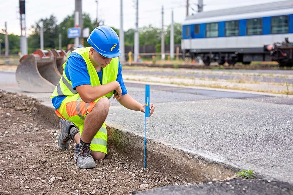 Lehre als Tiefbauer: Ein Lehrling in Arbeitskleidung vermisst den Höhenunterschied der Straße 