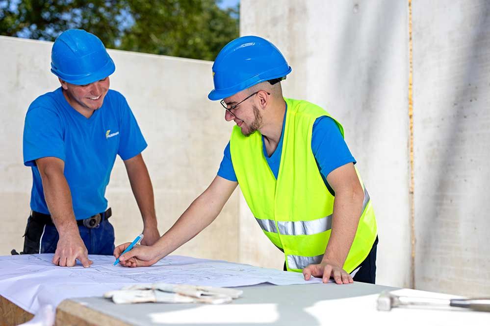 2 Lehrlinge sehen sich einen Plan auf der Baustelle an 