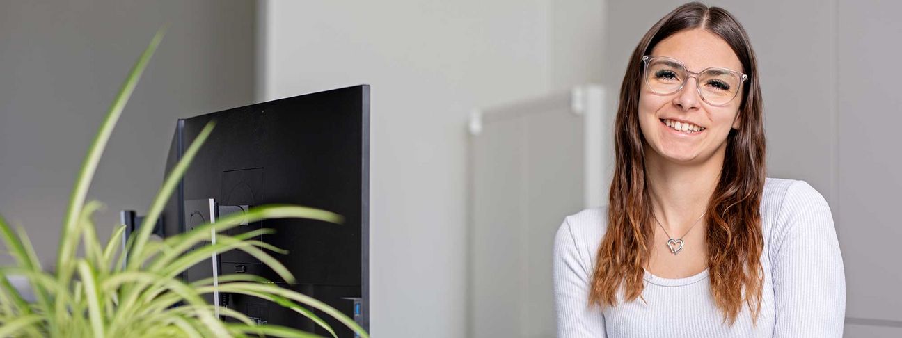 Lehre als Bürokauffrau / Bürokaufmann: Ein Lehrling im Büro sitzt lachend vor dem Computer