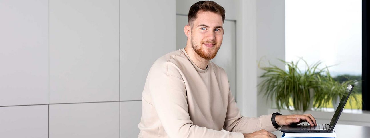 Lehre Finanz- und Rechnungswesen: Ein Lehrling arbeitet am Laptop und sieht in die Kamera 