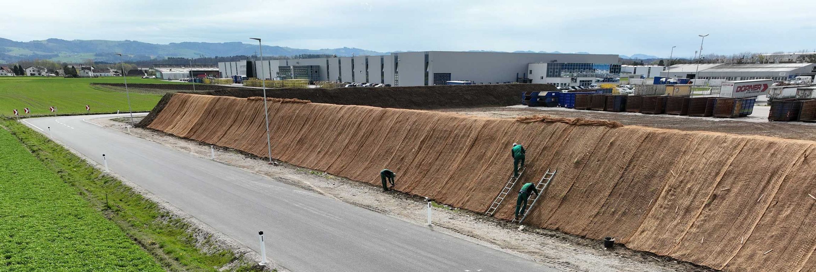 Biologisch abbaubares Kokosgeflecht und Arbeiter auf Leitern, die das Geflecht anbringen.