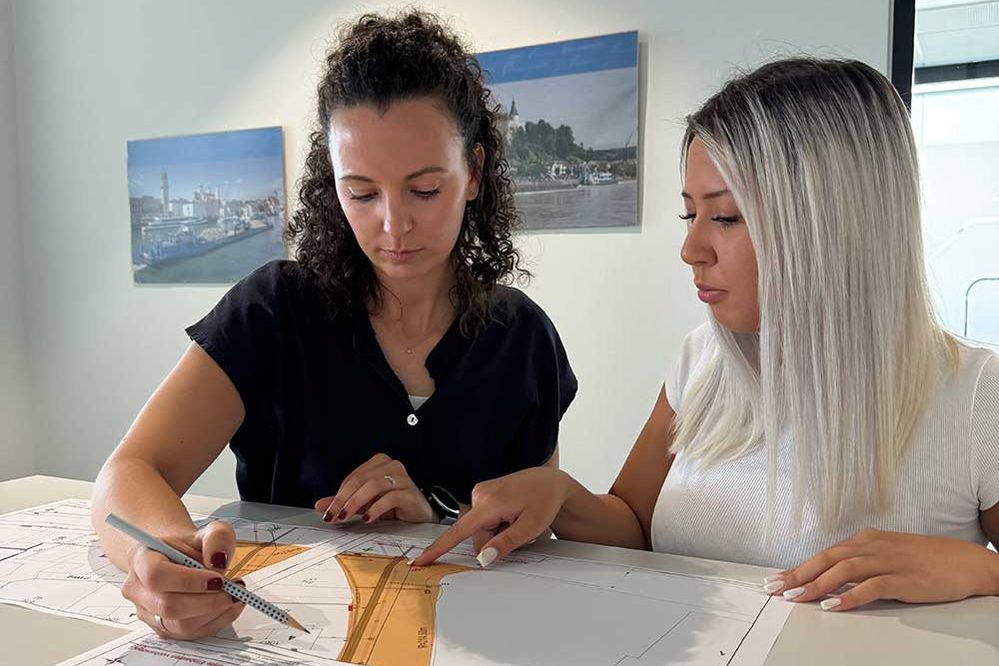 Eine Mitarbeiterin und ein Lehrling sehen sich einen Plan an  