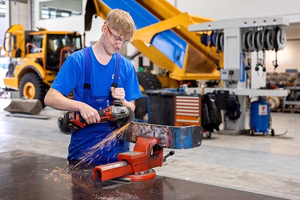 ein Lehrling bearbeitet ein Metallstück mit einer Akkuflex in der Werkstatt