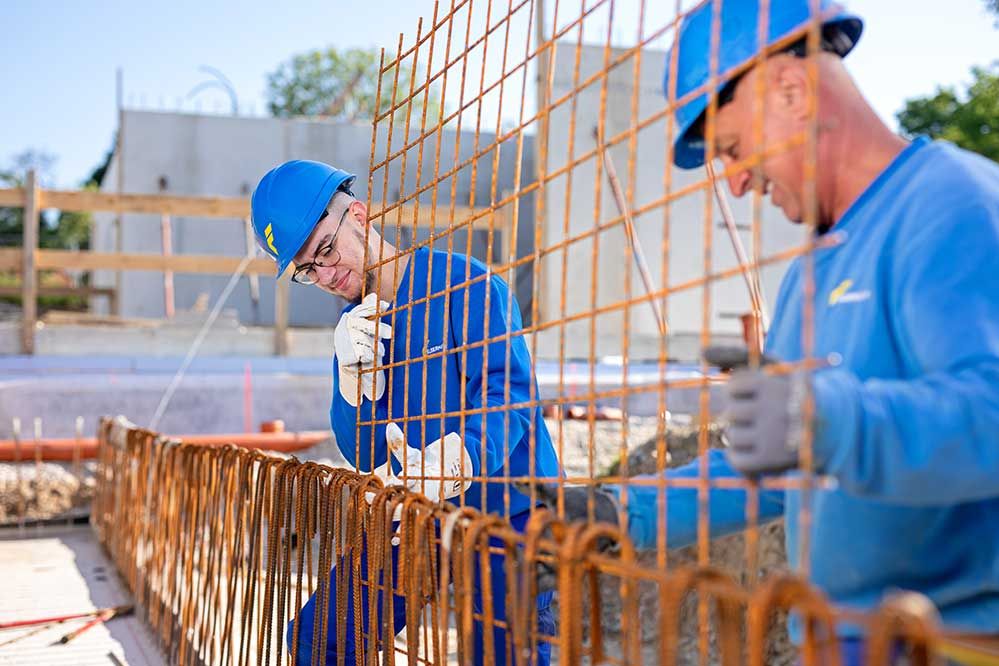 Lehre als Betonbauer: Ein Lehrling und ein Mitarbeiter ontieren ein Gitter auf einer Baustelle