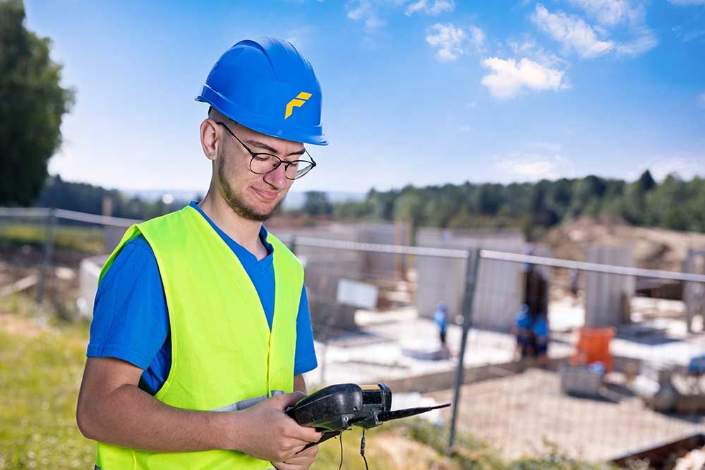 Ein Lehrling mit Bauhelm auf einer Baustelle beim Steuern einer Drohne