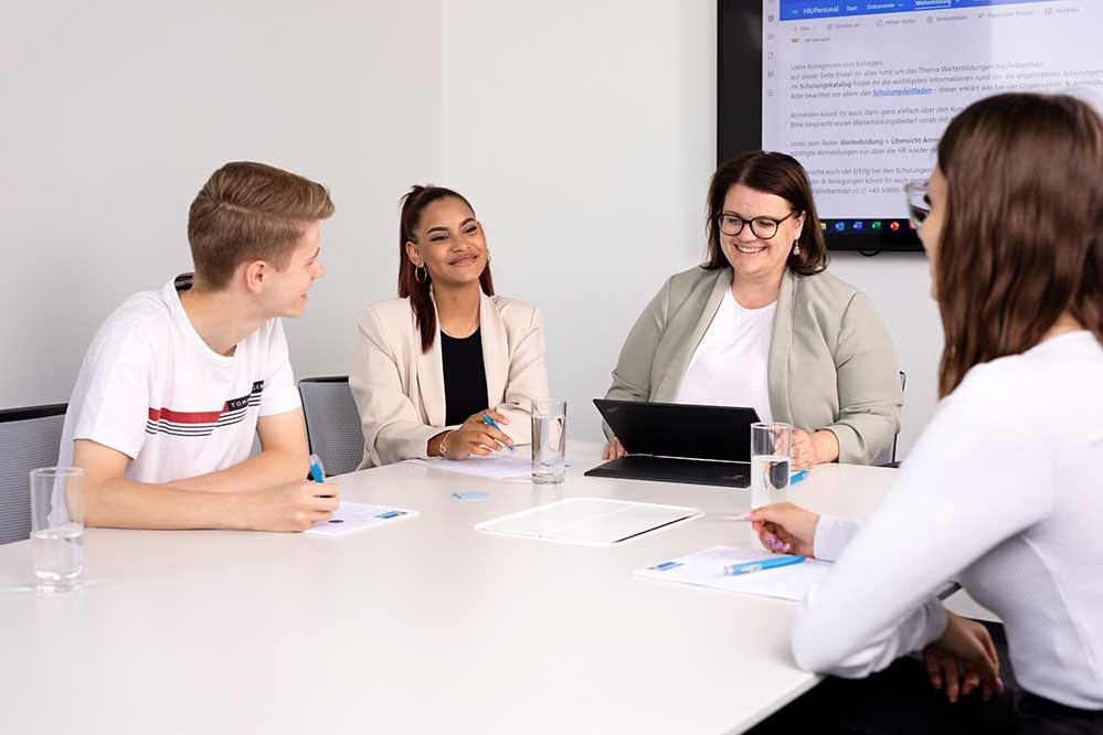 3 Lehrlinge haben eine Besprechung mit einer Mitarbeiterin im Besprechungsraum