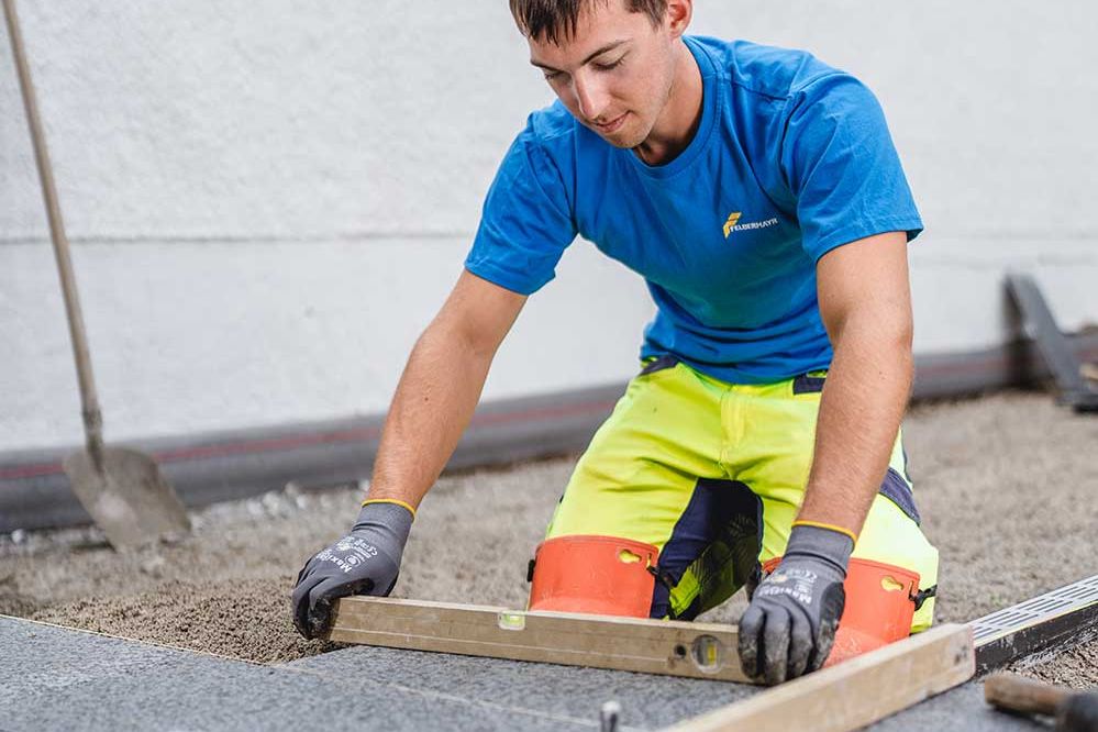 Lehre als Pflasterer: Ein Lehrling kontrolliert mit einer Wasserwage ob er gerade Gepflastert hat 