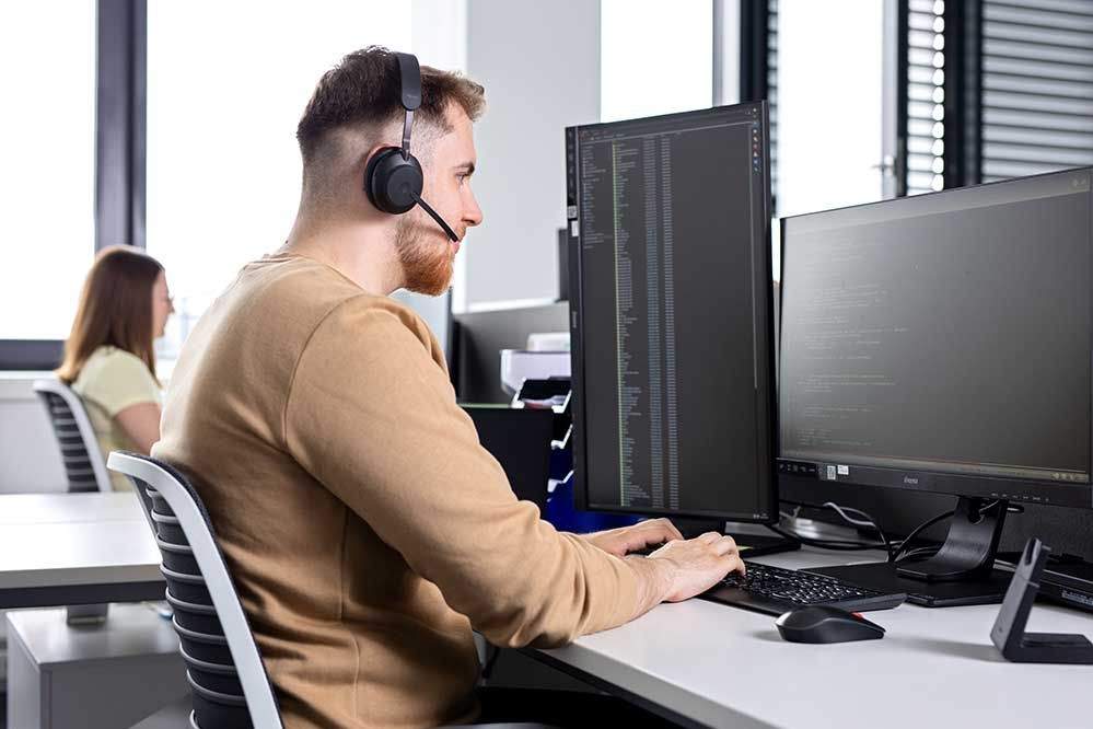 Ein Lehrling sitzt mit einem Headset vor dem Computer und telefoniert