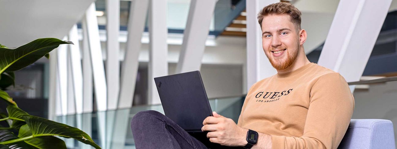 Lehre als IT Systemtechniker: Ein Lehrling sitz mit einem Laptop auf einer Couch am Gang