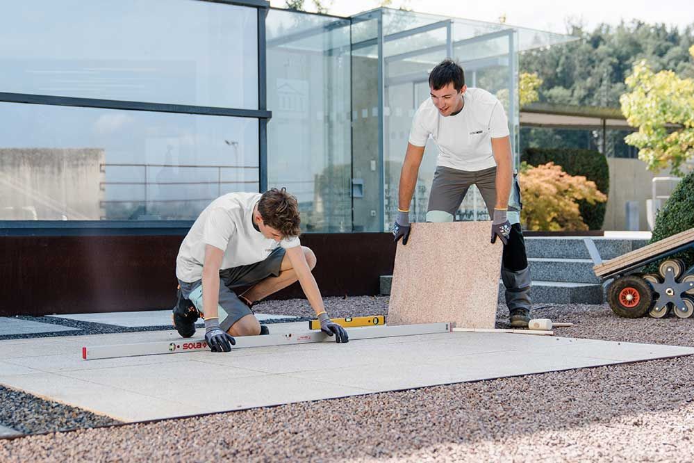 2 Lehrlinge verlegen draußen einen Boden aus Steinplatten 