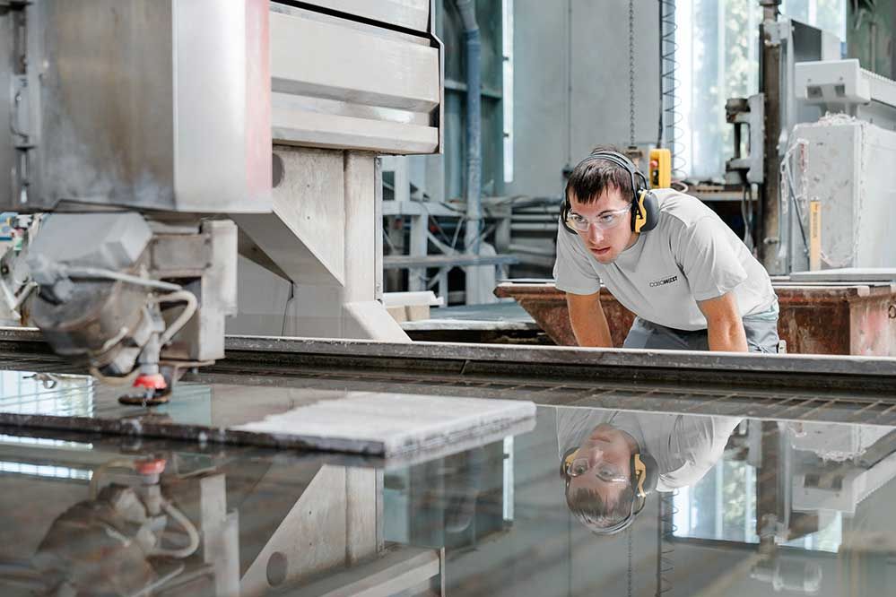 Ein Lehrling siet zu wie die Maschine einen Stein schneidet