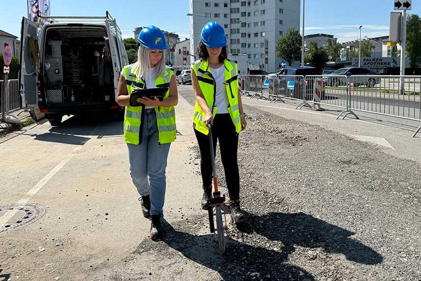 2 Lehrlinge mit Warnwesten vermessen die Baustelle