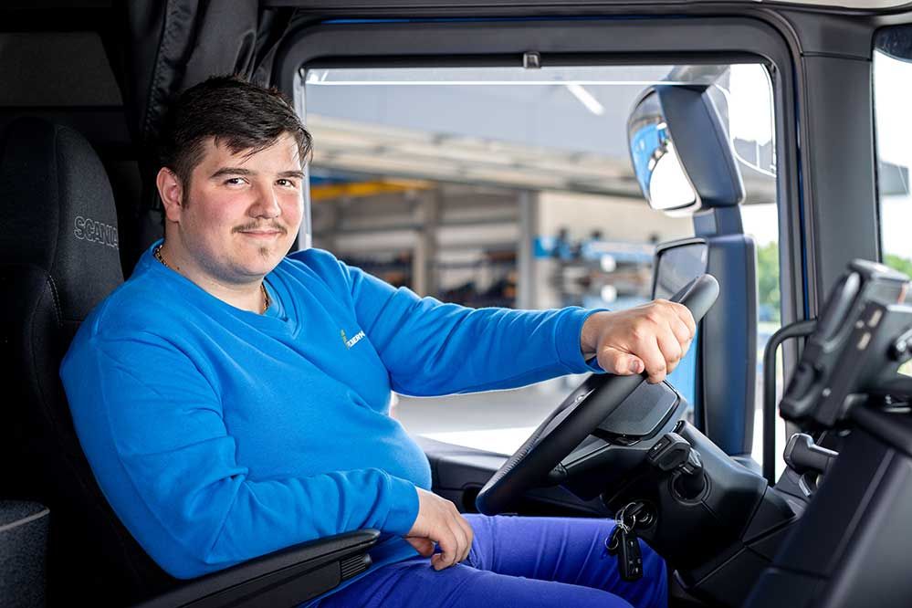 ein Lehrling sitzt in einem LKW und lächelt in die Kamera