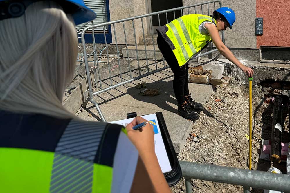 Ein Lehrling beobachtet einen anderen Lehrling beim Ausmessen einer Baugrube