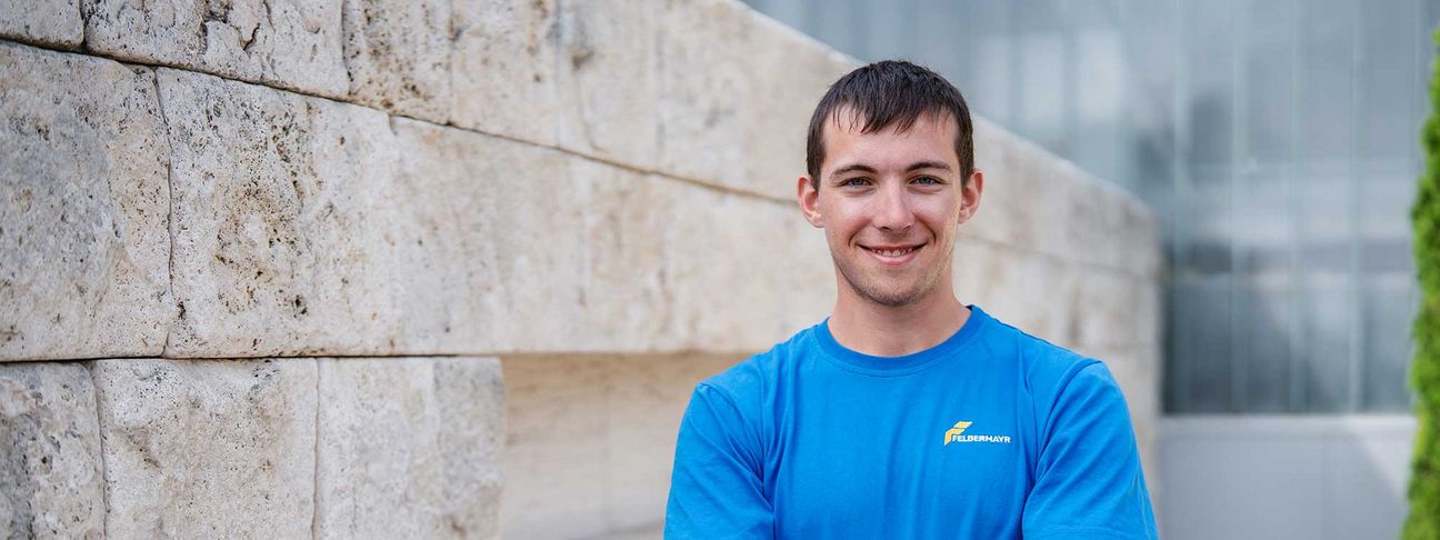 Lehre als Pflasterer: Ein Lehrling steht vor einer Mauer und lächelt in die Kamera 