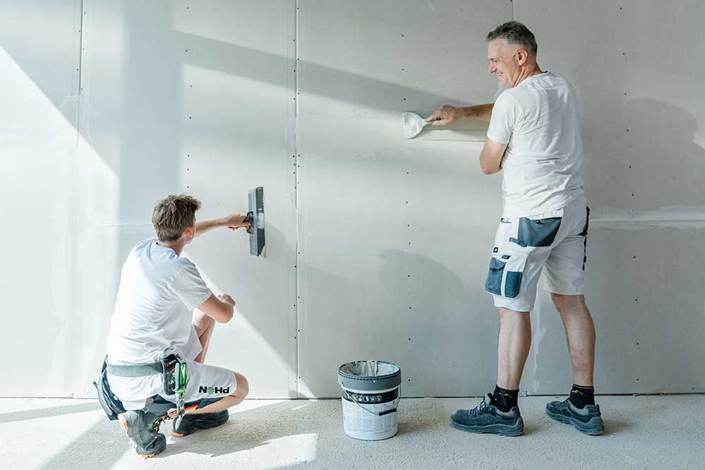 ein Lehrling und ein Mitarbeiter verspachteln die Wand