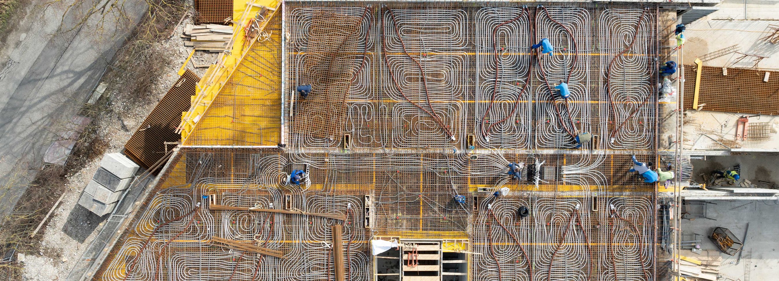 © Felbermayr/Weickinger Luftaufnahme einer Baustelle mit dicht verlegten Rohrleitungen für eine Betondecke und mehreren Personen, die an der Konstruktion arbeiten.